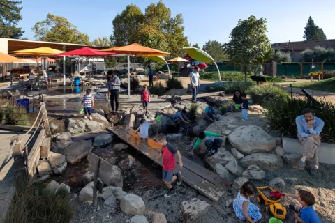 Vista del exterior del Museo Infantil del Condado de Sonoma, con niños y padres jugando con las exposiciones interactivas del Jardín de Mary.