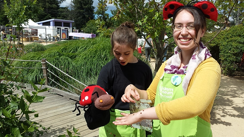 A Children's Museum staffer holding the Ladybug Mascot and a bunch of Ladybugs in Mary's Garden
