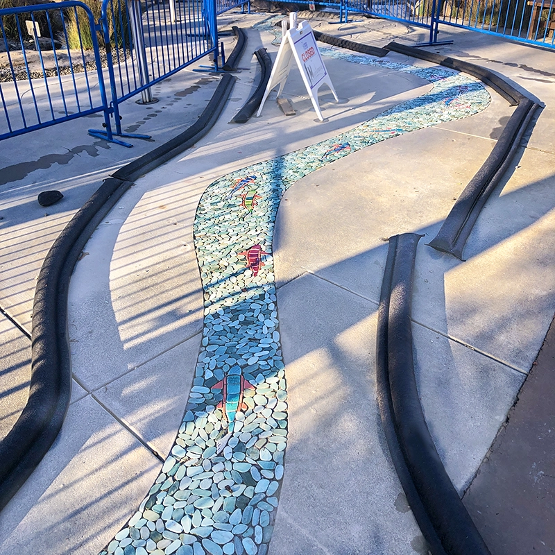 Un hermoso mosaico fluvial de aguas azules impresionantes con peces de vivos colores naranjas y verdes, realizado por la artista local del condado de Sonoma, Angelica Duckett, e instalado en el Museo Infantil del Condado de Sonoma.