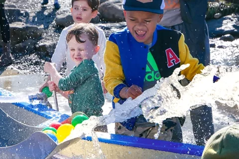 Tres niños pequeños juegan felices con la exposición acuática Mechanical Waterways 2.0 en el Museo Infantil del Condado de Sonoma.