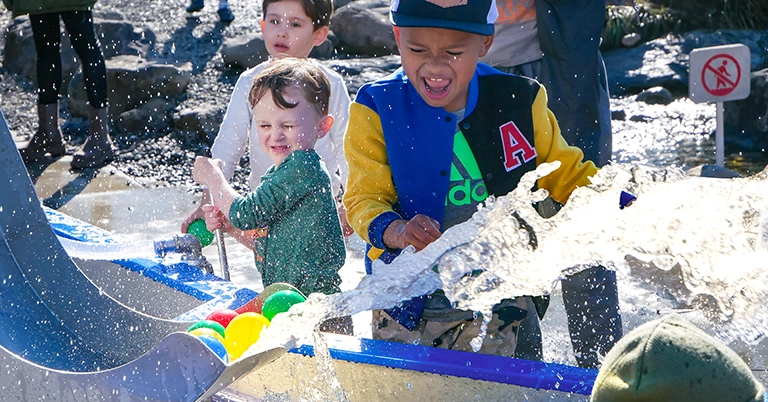 Three young children happily playing with the Mechanical Waterways 2.0 Waterplay Exhibit at the Children's Museum of Sonoma County