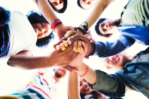 a group of happy, friendly people putting their hands in the middle of a huddle as a gesture of positive team work