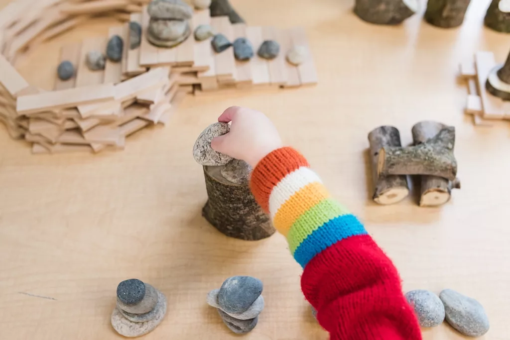A toddler playing with building blocks, stones, and wood piece