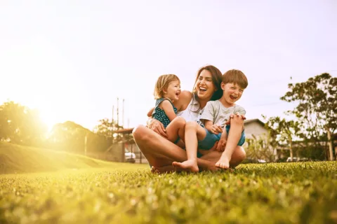 Mother with two young children sitting on the grass laughing and playing