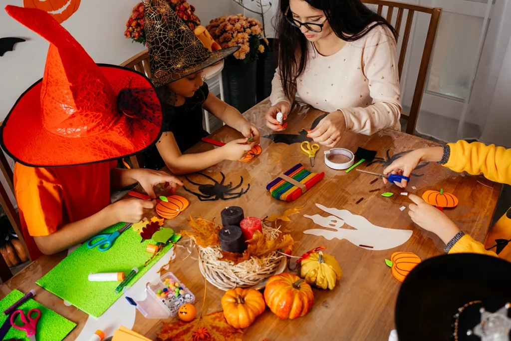 A group of children in Halloween costumes sitting at a kitchen table doing arts and crafts activities for kids