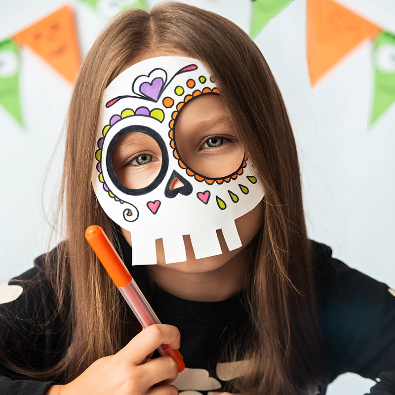Niño pequeño con una máscara de esqueleto hecha con platos de papel durante una actividad de manualidades de Halloween para niños.