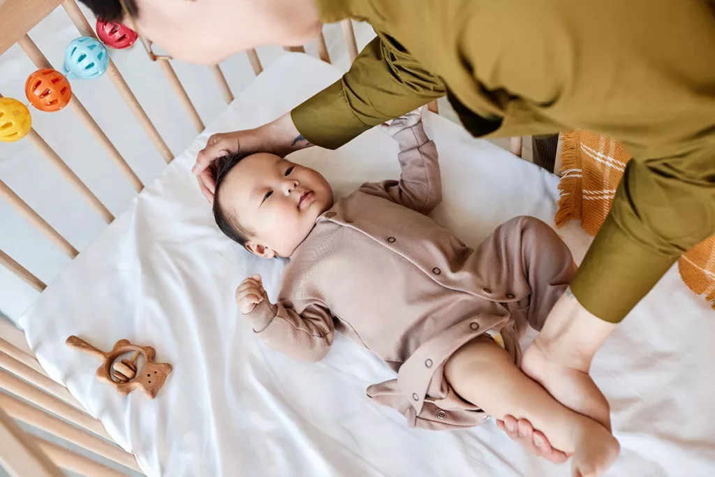 A baby, less than one years old, happily being laid down in their crib for a nap by a parental figure.