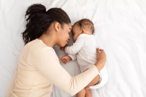 Una madre y su bebé recién nacido duermen juntos la siesta en la cama de la madre.