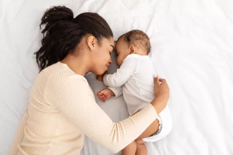 A mother and newborn baby napping together in the mother's bed.