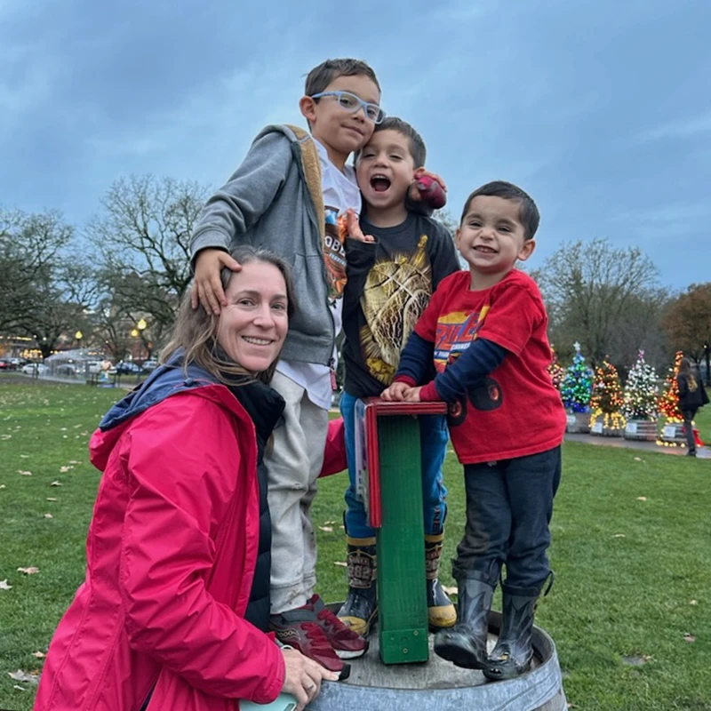 Tres niños pequeños y su tutor adulto sonríen y miran a la cámara para una foto de familia dulce y saludable.