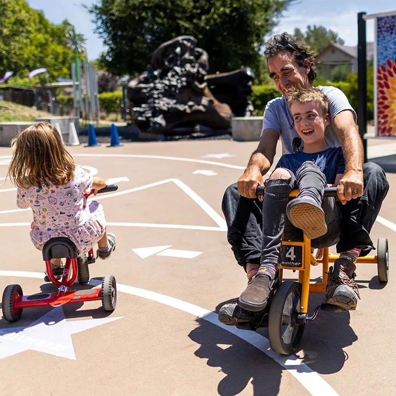 A child and their adult guardian laughing and playing together on the Bike Track at the Children's Museum of Sonoma County in Santa Rosa, Ca.