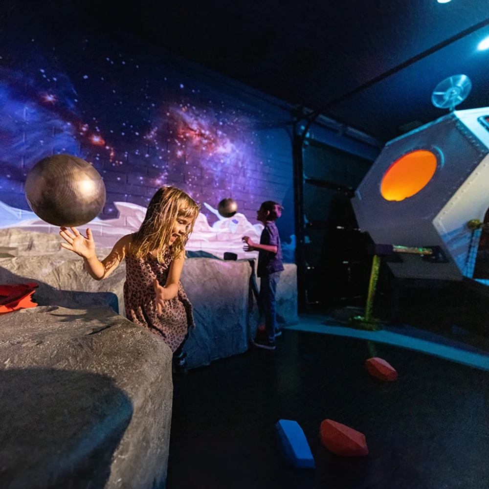 A child laughing and playing with an interactive space-themed exhibit called the Space Odyssey for Galactic Explorers exhibit at the Children's Museum of Sonoma County in Santa Rosa, Ca.