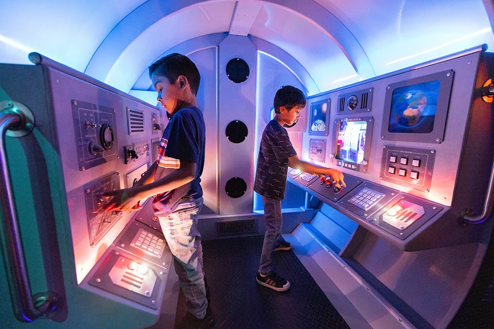 Dos niños juegan en una exposición interactiva de temática espacial llamada Odisea del espacio para exploradores galácticos.