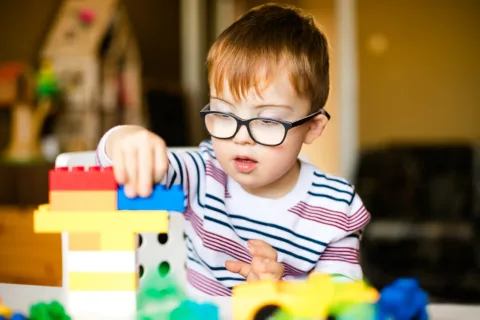 An independent play for toddlers concept; a toddler wearing eyeglasses happily playing with building blocks