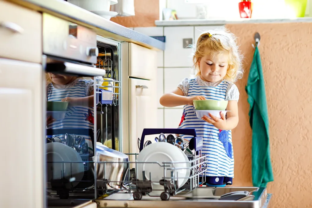 Toddler Practicing Independence Skills at Home by putting their own dishes in the dishwasher after snack time
