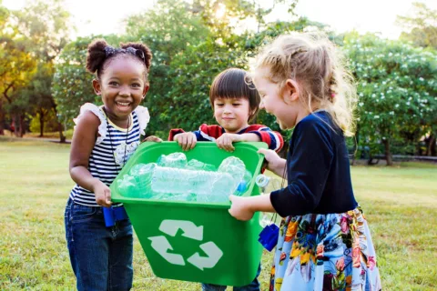 Three young children happily carrying a recycling bin