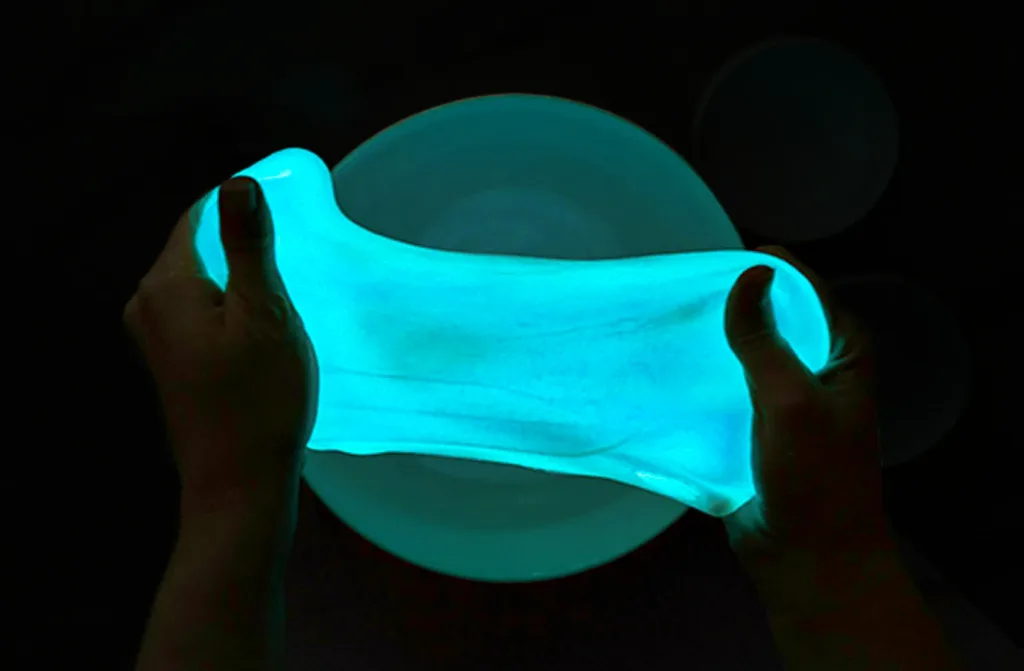 An aerial view looking down at 2 hands stretching glow-in-the-dark slime, doing a Halloween Science Experiments for Kids.