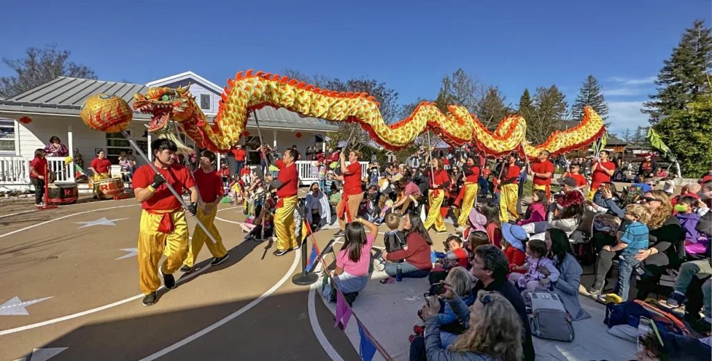 Varios artistas llevan una larga marioneta de dragón y realizan una danza tradicional del dragón para celebrar el Año Nuevo Lunar, mientras un numeroso público compuesto por niños y familias observa el festival anual del Año Nuevo Lunar del Museo Infantil del Condado de Sonoma.
