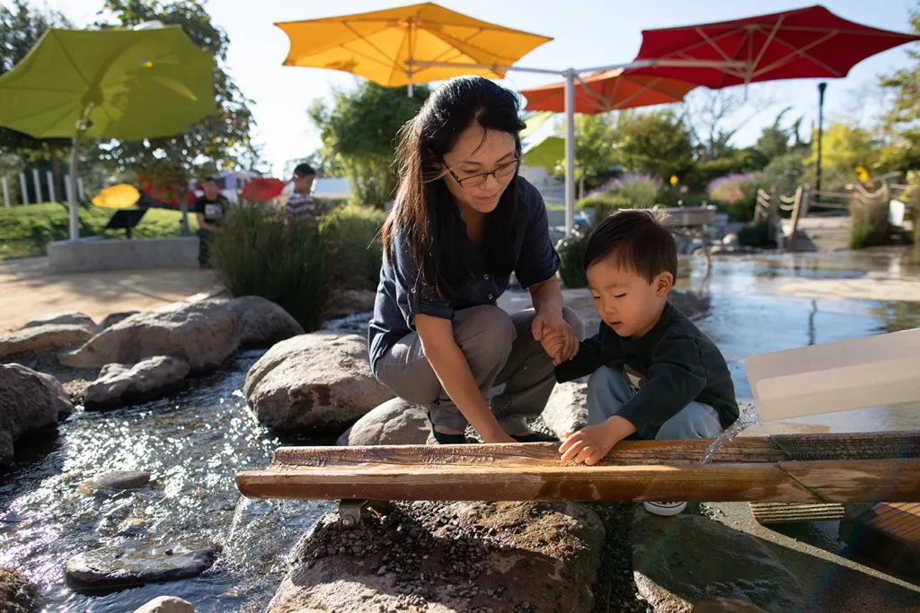 A parent and young child playing at the Children's Museum of Sonoma County, exploring the concepts of water flow at an outdoor water exhibit