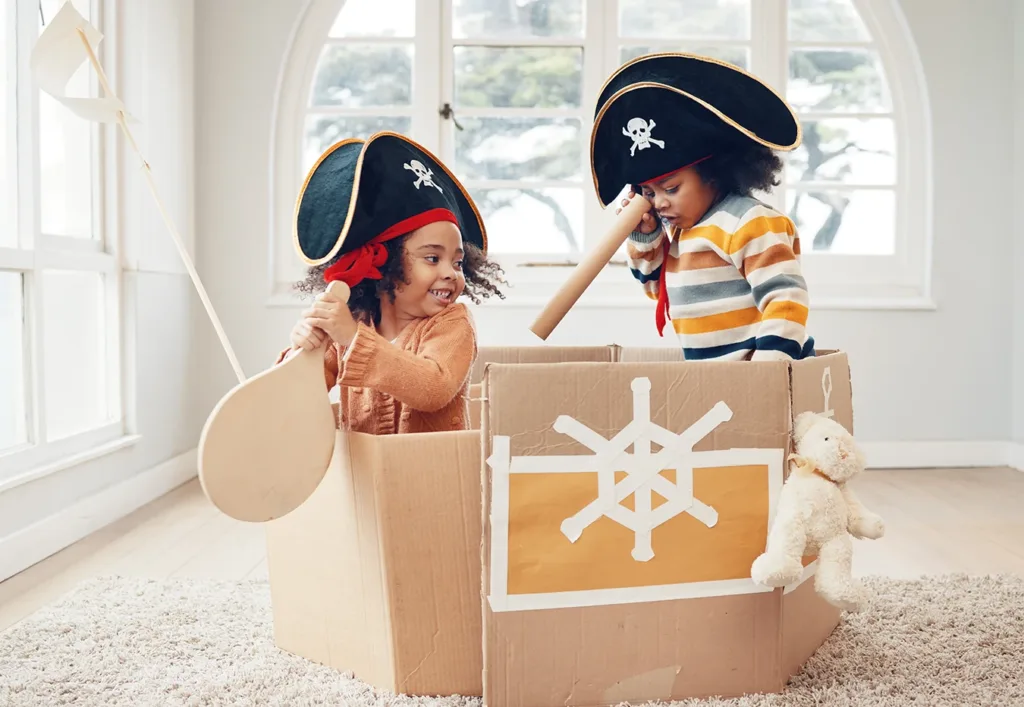 Actividad artística de reciclaje creativo para niños: dos niños pequeños juegan a ser piratas en una caja de cartón reconvertida en un barco pirata de juguete.