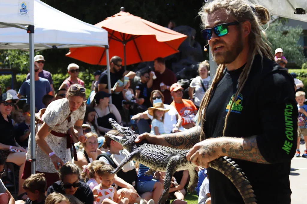 A Wine Country Zoological team member holding a real crocodile while a large group of children and caregivers sit and stand around them listening to them talk about cool crocodile facts. Picture taken at the 2025 Dino Trax event at the Children’s Museum of Sonoma County in Santa Rosa, CA.