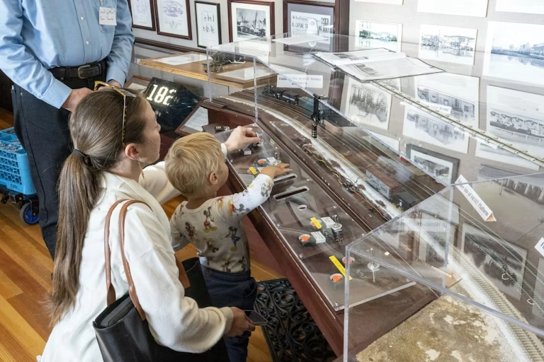 A young child and their caregiver playing with the interactive train display at the Northwestern Pacific Railroad Museum located inside the Santa Rosa Welcome Center in Downtown Santa Rosa, CA.