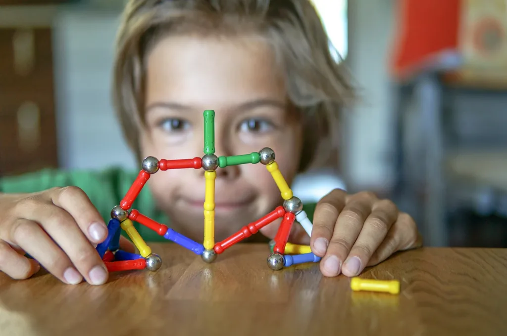 A close up photo of a young child carefully building a structure out of colorful magnetic building blocks.