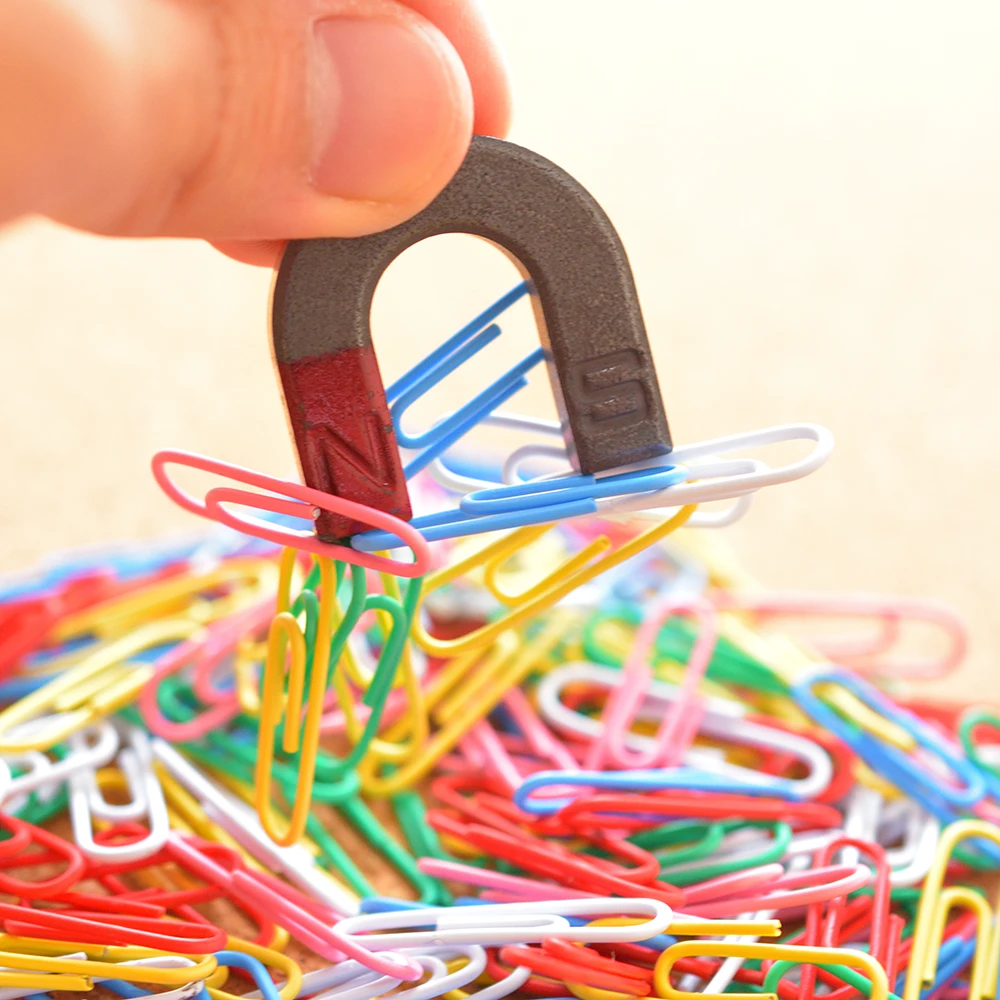 Una foto en primer plano de un niño sosteniendo un imán en forma de herradura sobre una pila de clips, lo que demuestra claramente cómo un imán permanente (el imán en forma de herradura) convierte los clips en imanes temporales.