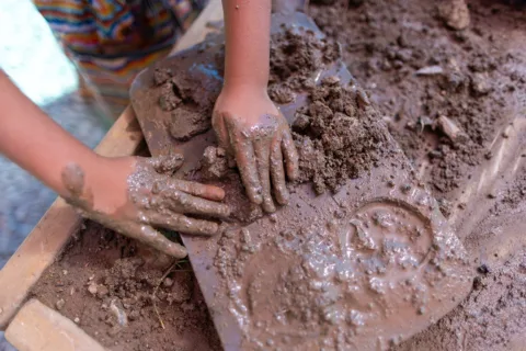 Un niño pequeño que pone lodo en un molde para cupcakes en la exposición al aire libre llamada «Mud Lab» en el Museo de los Niños del Condado de Sonoma.