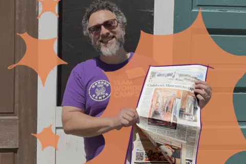 Museum staff holding newspaper highlighting the children's museum expansion